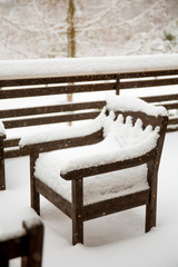 Fresh clean snow covering brown wooden Mahogany color stained garden chairs and table on home balcony. Garden furniture maintenance after cold winter concept.