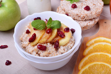 Porridge with caramelized apples and dried cranberries topped with mint surrounded by breakfast ingredients
