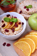 Porridge with caramelized apples and dried cranberries topped with mint surrounded by breakfast ingredients
