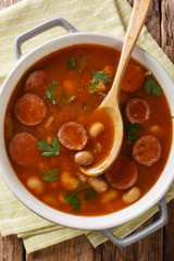 Delicious Polish dish of Breton beans with sausage close-up in a saucepan. Vertical top view