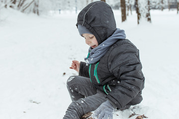 Fototapeta na wymiar A little boy of 5-7 years old is playing outside in the snow in a park in winter.