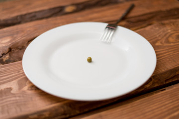 Diet concept. One pea lying on a white plate. Restriction in nutrition.