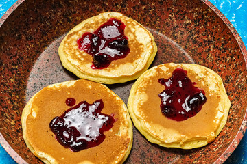 Three pancake in a frying pan, doused in raspberry jam. Baking sweet and delicious dessert ready to eat