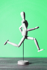 Wooden mannequin running. Green background.