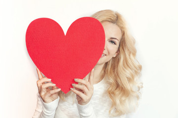 Portrait of smiling young blond woman with big red heart on white background. Love concept