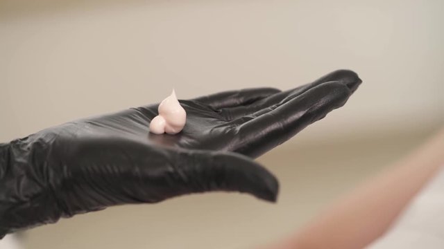 A Close-up Of Two Woman's Hands In Black Gloves Holding A Tube With Cream, And One Hand Squeezes It Onto The Open Palm Held Horizontally