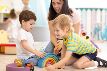 Preschool teacher with children playing on floor with colorful wooden toys at kindergarten