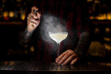 Bartender sprinkling elegant cocktail glass with alcoholic drink with bitter in dark
