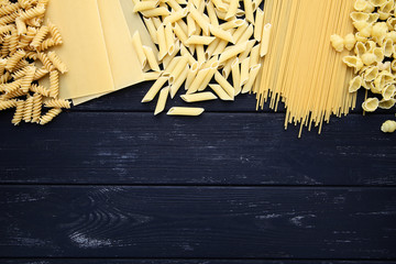 Different uncooked pasta on black wooden table