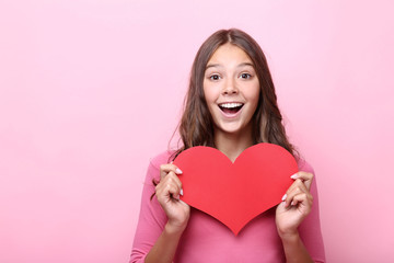 Young girl holding red paper heart on pink background
