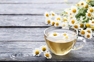 Cup of tea with chamomile flowers on grey wooden table