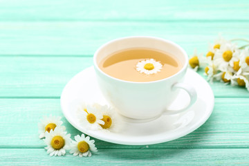 Cup of tea with chamomile flowers on mint wooden table