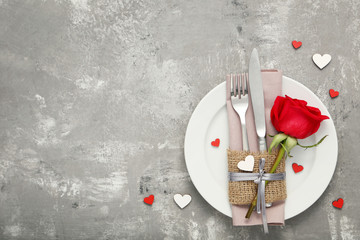 Kitchen cutlery with red rose in white plate on wooden table