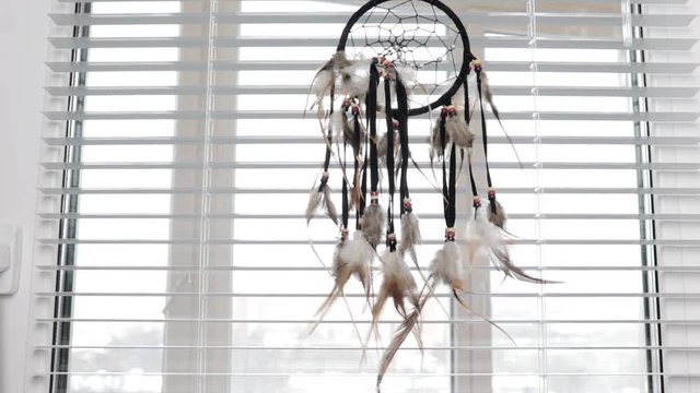 Dream protection amulet dreamcatcher of bird feathers hanging on the window with blinds in the morning, serene dreams talisman