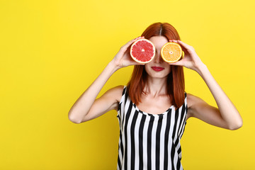 Beautiful redhaired woman with citrus fruits on yellow background