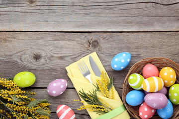 Kitchen cutlery with easter eggs and mimosa flowers on grey wooden table