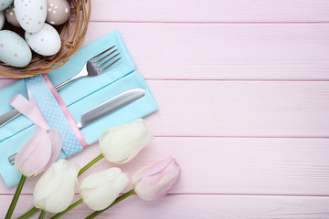 Kitchen cutlery with easter eggs and tulip flowers on pink wooden table