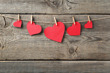 Red paper hearts hanging on wooden background