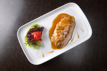 Fried chicken fillet, sliced, with vegetables, sauce, on a board, on a white plate. Top view