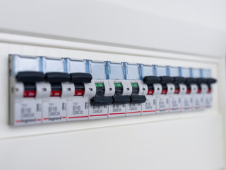 Switches in electrical fuse box. Many black circuit breakers in a row in position ON and three switch in position OFF. Power control panel.