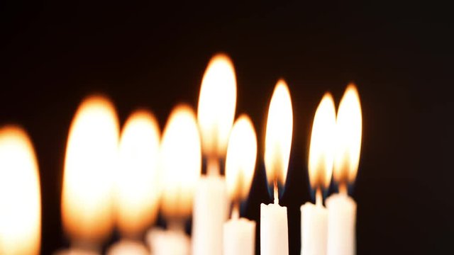 Rack focus detail shot of the flames on a row of nine white candles burning on the Jewish holiday of Hanukkah