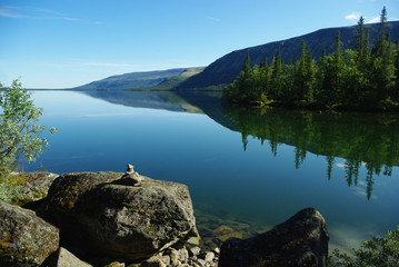 Seidozero lake. Stones in the foreground. In the background, calm outlines of low mountains and green fir trees on the shore.