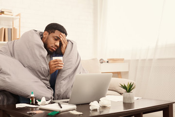 Sick african-american man working on laptop at home