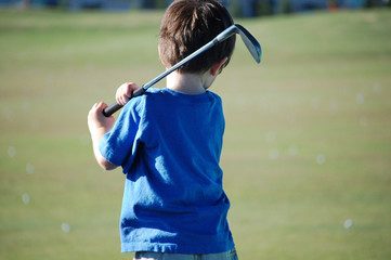 Young boy back view swinging golf club on the golf course.