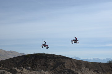 Two motocross riders in mid jump, side view at dirt track.