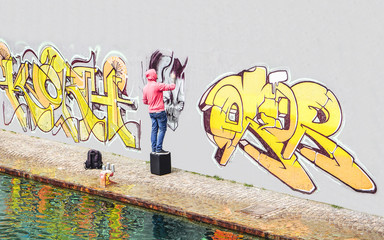Street graffiti artist painting with a color spray can a graffiti on the wall in the city - Concept...