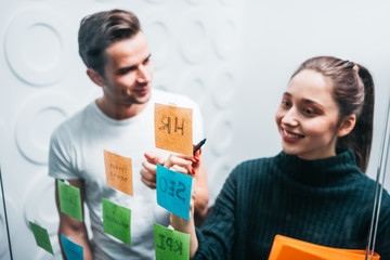 Smiling business man and woman having meeting and posted on sticky glass note wall. Coworker people create new ideas for startup