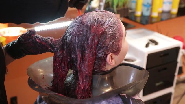 hairdresser paints locks of hair of the brunette with a brush in red color in black gloves, the stylist puts paint on hair of the girl