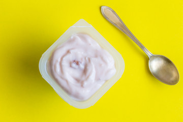 Yogurt cup with strawberry yoghurt and small silver spoon close up - Top view photo of yoghurt on yellow background