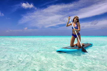 Sportliche Frau im Bikini auf einem SUP Board auf tropischen, türkisen Gewässern - obrazy, fototapety, plakaty