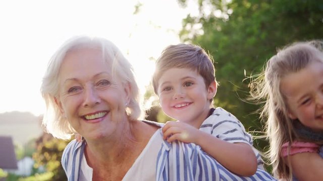 Portrait Of Smiling Grandparents Carrying Grandchildren Outdoors In Summer Park