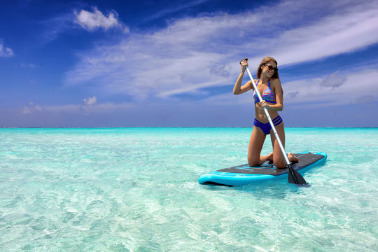 Sportliche Frau im Bikini auf einem SUP Board auf tropischen, t&uuml;rkisen Gew&auml;ssern