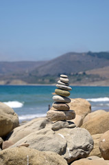Stack of rocks at the beach with ocean and mountain background.