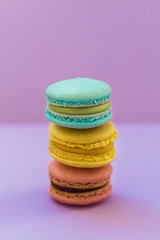 Sweet colorful French macaroon biscuits on violet purple background, top view. Flay lay selection of colorful macarons.