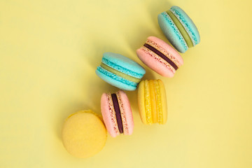 Sweet colorful French macaroon biscuits on yellow pastel background, top view. Flay lay selection of colorful macarons.