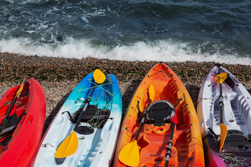 four multi-colored kayaks stand on the beach, on small pebbles, sea view, summer