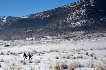 Cross country skiers on a groomed trail near the mountains.