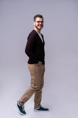 Full length portrait of a smiling young man walking isolated over gray background.