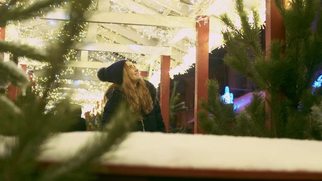 Young woman admires christmas lights in the street. Female looks at cafee decorations outdoors
