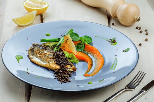 Seabass fish fillet stake cooked on a grill with healthy vegetables on a plate. Healthy seafood food on a   rustic wooden table.
