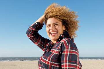 Side portrait of happy young african american woman laughing at the beach with hand in hair