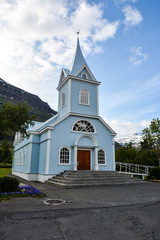 Fototapeta na wymiar A blue church in Seydisfjordur cityscape in East Iceland in summer on a cloudy day - vertical