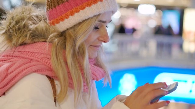 Young woman in winter clothes using her mobile phone in shopping center