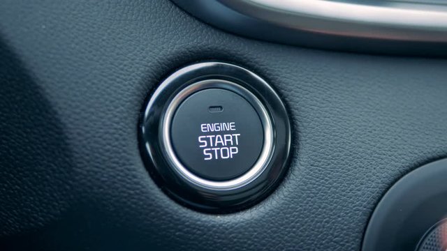 Fingers are pushing a start and stop button in a car