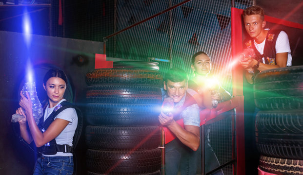 Smiling young friends playing laser tag  game with colored laser