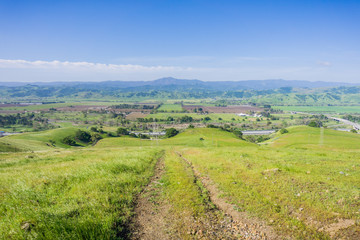 Fototapeta na wymiar Hiking trail descending into the valley; Aerial view of agricultural fields and mountains in the background, south San Francisco bay, San Jose, California